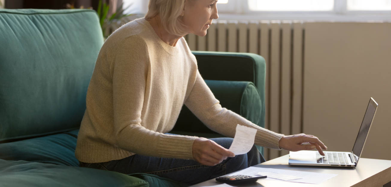 Dame sitter i en grønn sofa og betaler regninger på pc