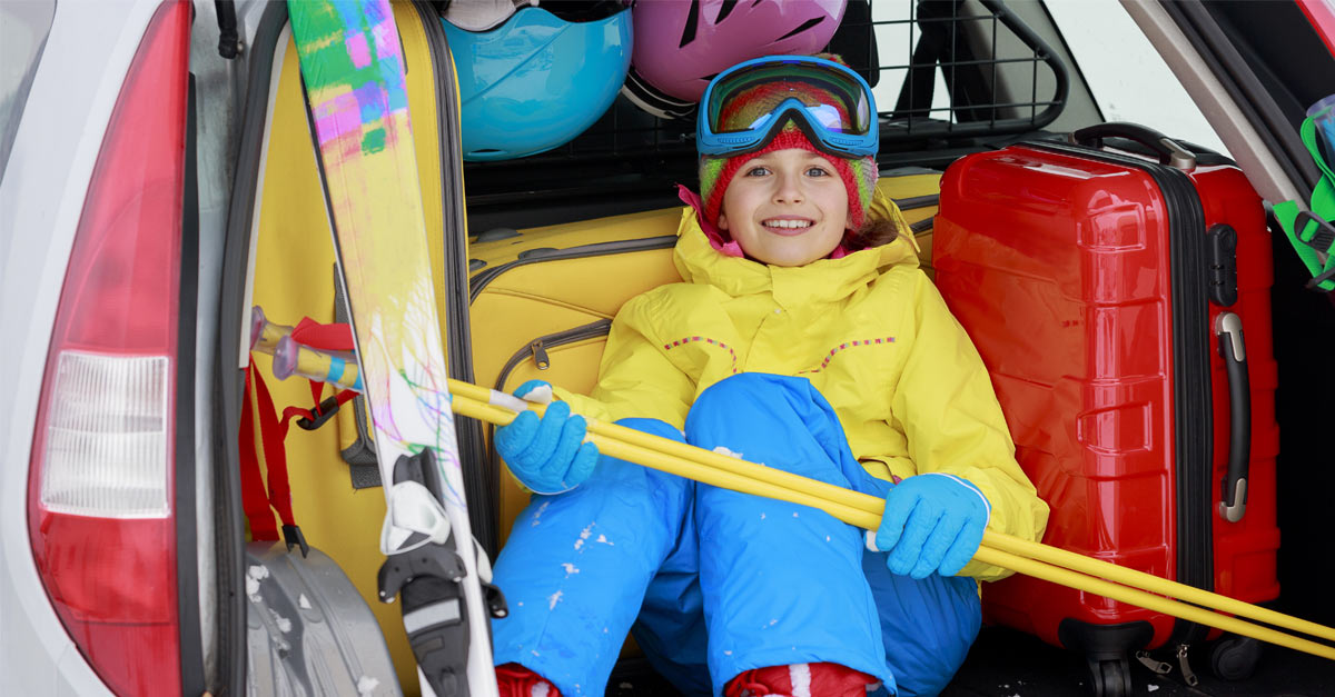 gutt i gult og blått slalomutstyr, sitter i bagasjerommet på en bil klar for påskeferie
