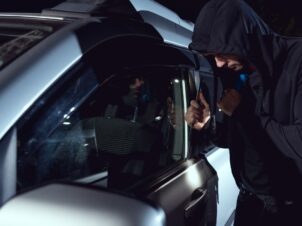 mann med mørk hettegenser og lommelykt bryter seg inn i en bil