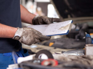 Mekaniker med hansker på, ser over reparasjonsskjema