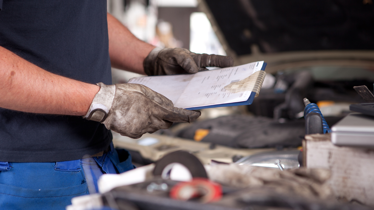 Mekaniker med hansker på, ser over reparasjonsskjema