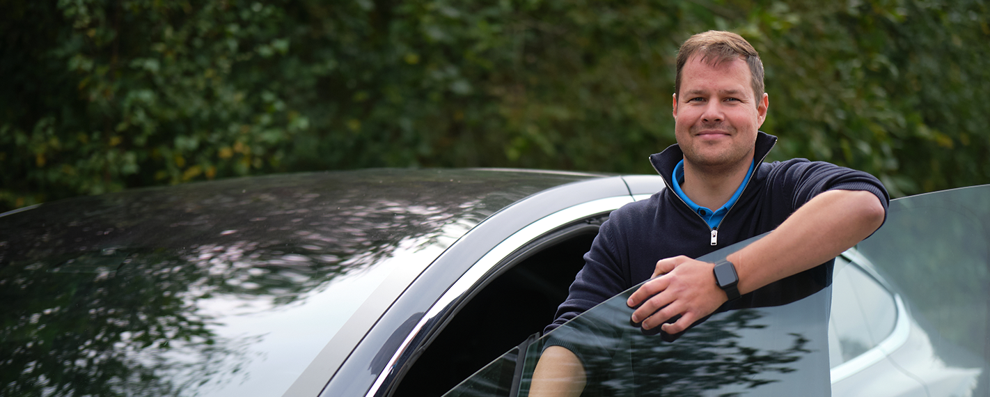 En fornøyd mann står i døren på sin Tesla etter at han byttet til Mekonomen og sparte 40.000 kr på reparasjon etter EU-kontroll.