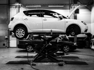 Hvit bil løftet på bukk inne på bilverksted