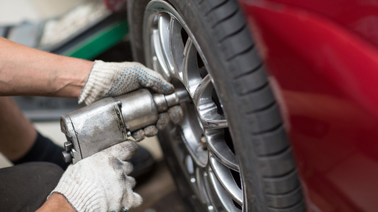 Dekkskift hos Mekonomen, mekaniker skrur til julbolter på rød bil.