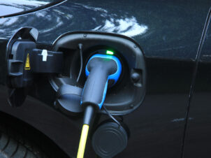 Den blå og sorte Elbilkontakten er plugget inn i ladekontakten på en mørkblå elbil