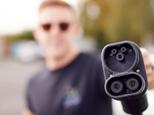 Mann med solbriller holder fram en ladekabel til elbil