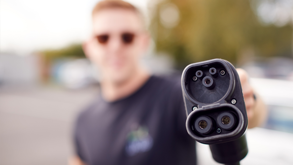 Mann med solbriller holder fram en ladekabel til elbil