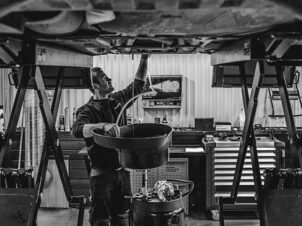 Sort/hvitt bilde av en bilmekaniker som tapper olje av en bil