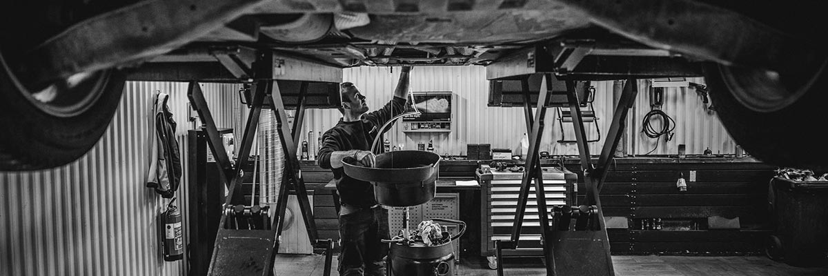 Sort/hvitt bilde av en bilmekaniker som tapper olje av en bil