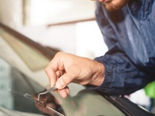 Mekaniker med skjegg og blå kjeledress reparerer steinsprutskade på frontruten