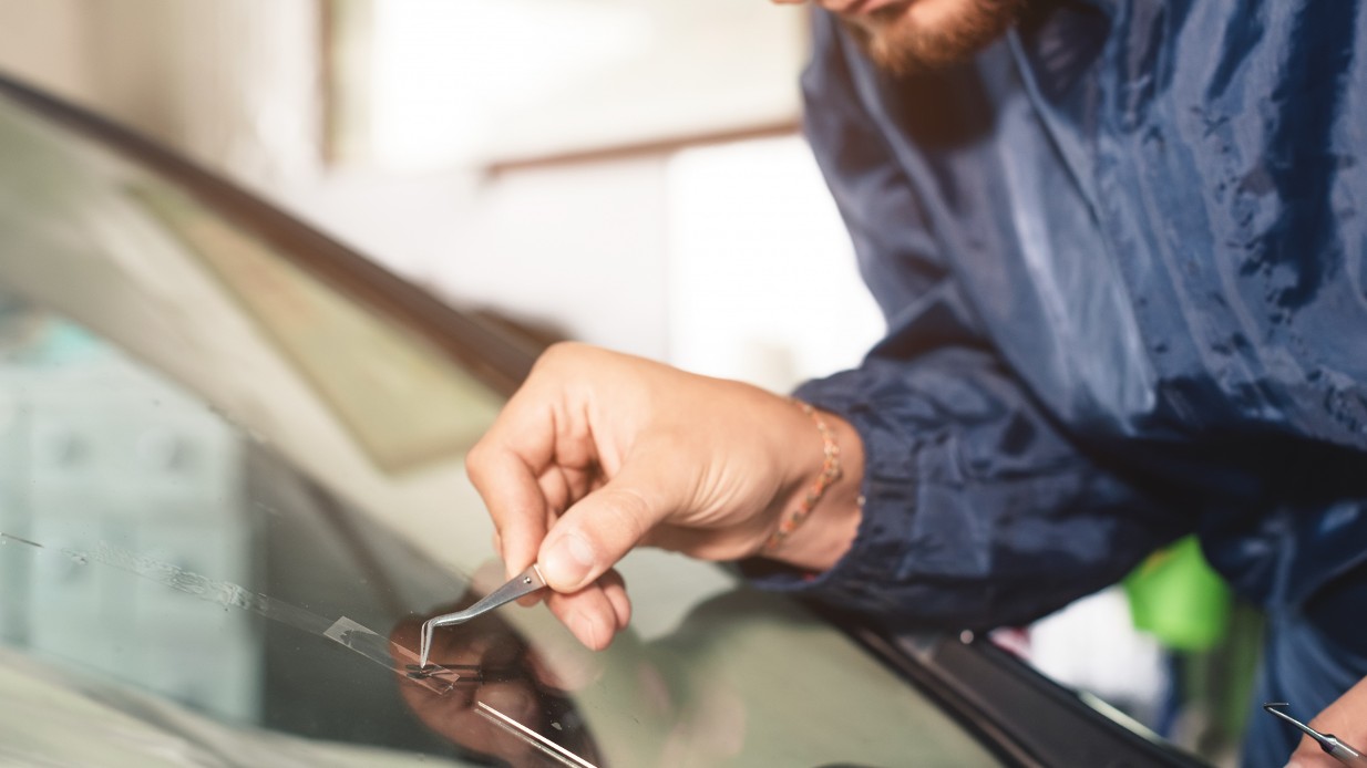 Mekaniker med skjegg og blå kjeledress reparerer steinsprutskade på frontruten