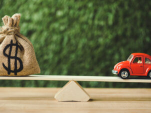 Vippehuske med en liten rød bil på ene siden og en stor pengesekk på andre siden