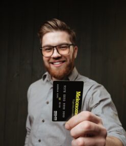 Ung mann med briller og skjegg, smiler og holder Mekonomen bilkonto-kort
