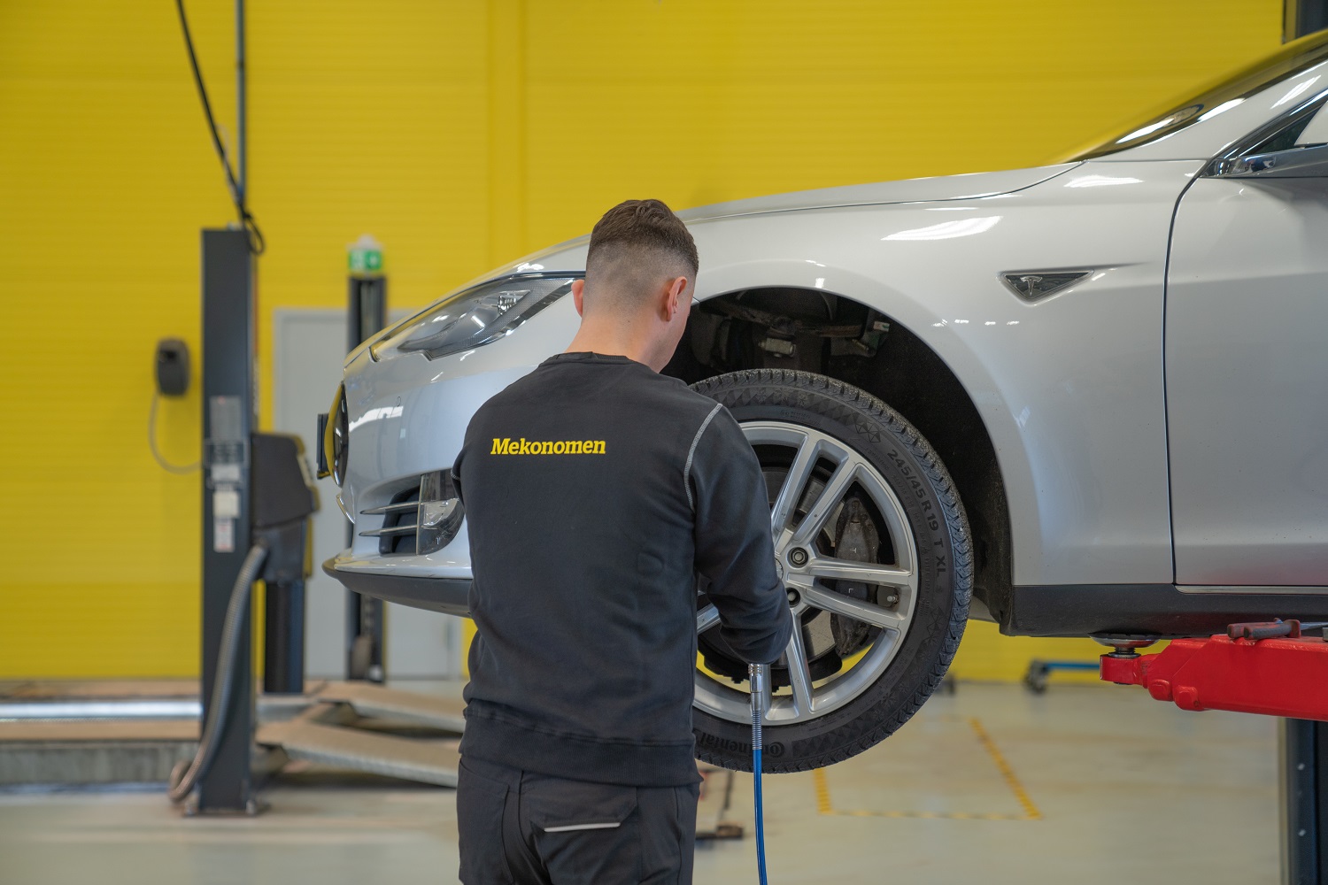 Mekaniker skifter dekk på en bil på et Mekonomen verksted (gul vegg)
