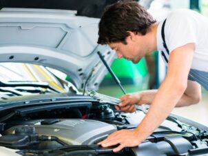 mekaniker titter ned i motorrommet på en bil, når han skal ta service