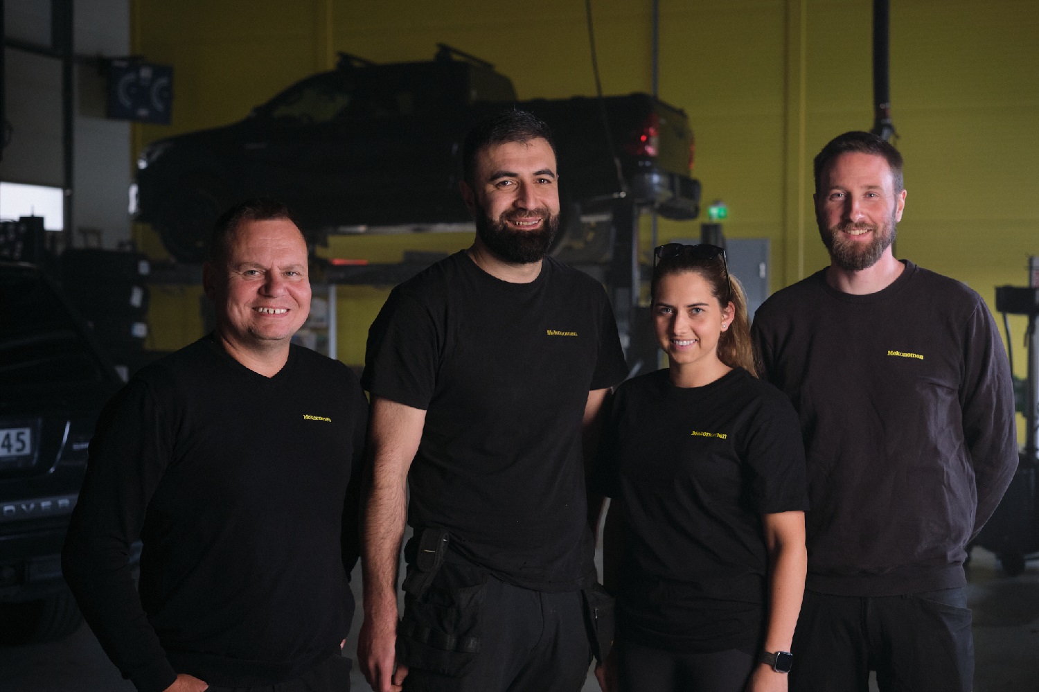 Fire Mekonomen mekanikere i svart t-skjorte. 1 dame og 3 menn