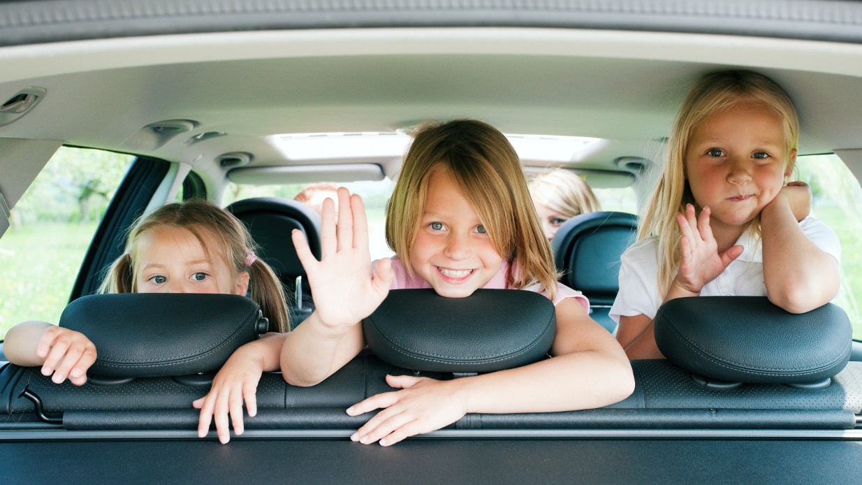 Bilferie - 3 glade barn vinker bakover fra baksetet på bilen.